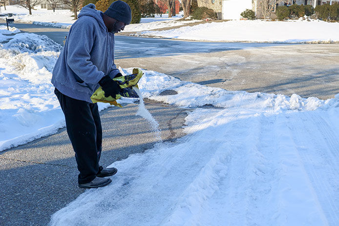 Man pouring a bag of ice melt on an icy driveway