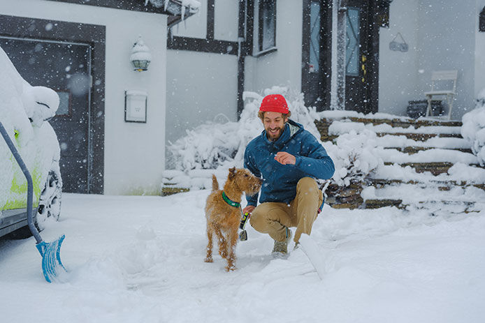Man with a dog by a house near a driveway with snow
