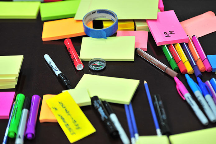 A close up image of office supplies, sticky notes, pens, and markers