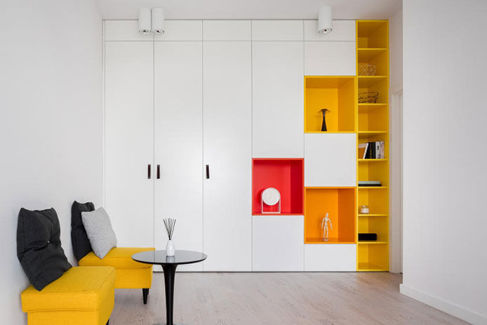 Small, white living room with yellow, orange, and red shelves