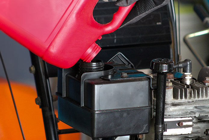 Person pouring gas into a snow blower tank from a red container