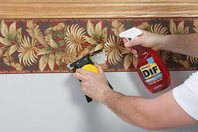 A man using Zinsser DIF wallpaper remover to remove a red feathered wallpaper boarder underneith a chair rail 