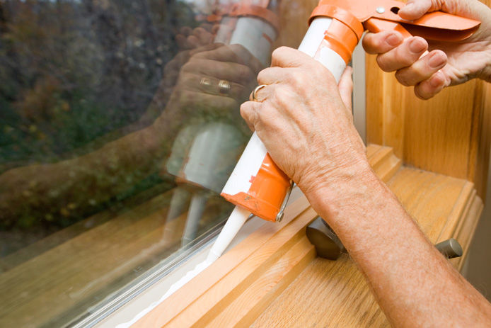 a person sealing a window with sealant