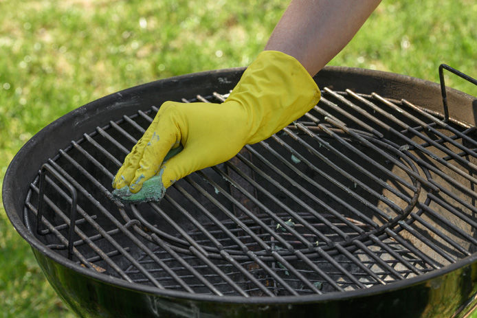 person cleaning a BBQ grill with gloves