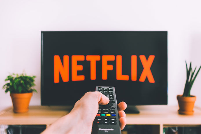 A person pointing a remote at a TV with Netlix on it