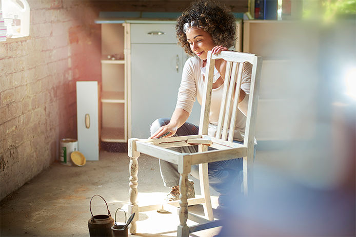 Woman sanding down a kitchen chair in her basement