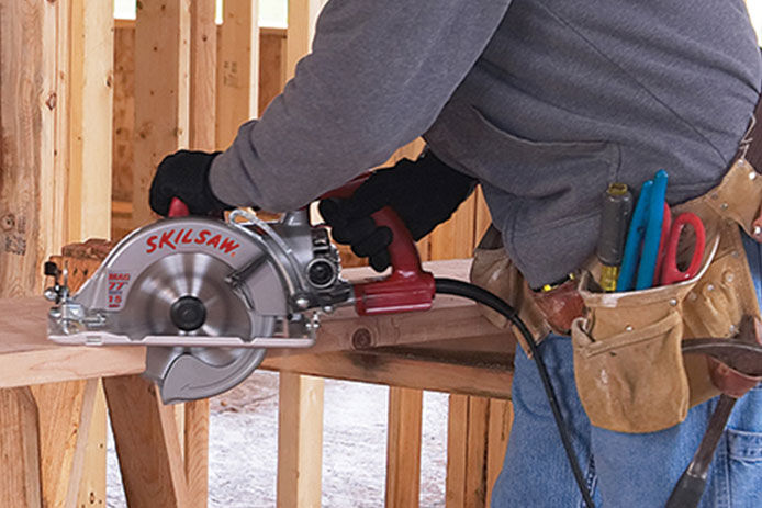 A man using a SKILSAW circular saw at a construction site to cut through 2x4s