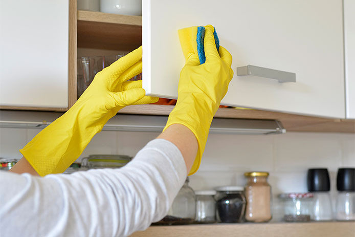 Wiping a cupboard down with a sponge