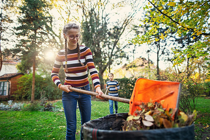 A girl dumping leaves into a trash can