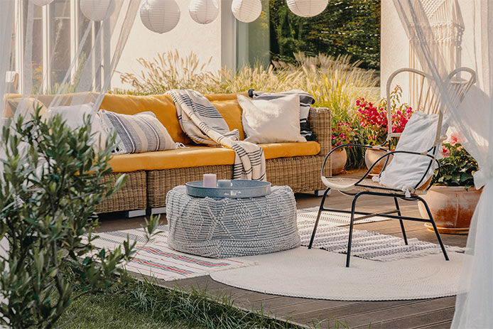 Outdoor terrace with an armchair, pouf used as a table, and wicker couch, providing comfortable seating options for relaxation and enjoying the outdoors.