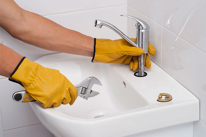 Man wearing yellow work gloves replacing the faucet to the sink