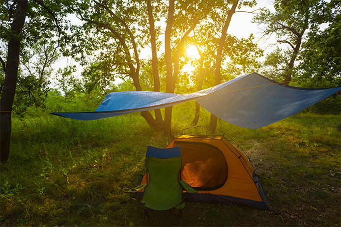 A beautiful sunset over a camp site. There is a blue tarp above a orange tent with a green camping chair sitting outside the opening of the tent