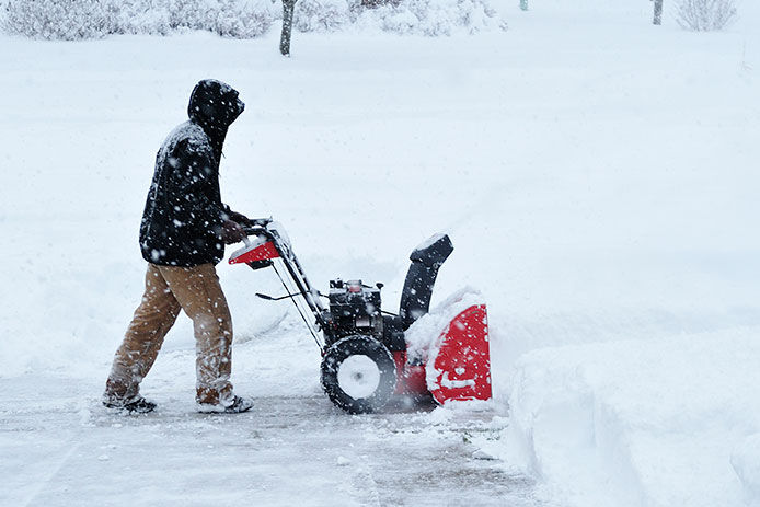 Man bundled up pushing a snow blower up his driveway while is is snowing