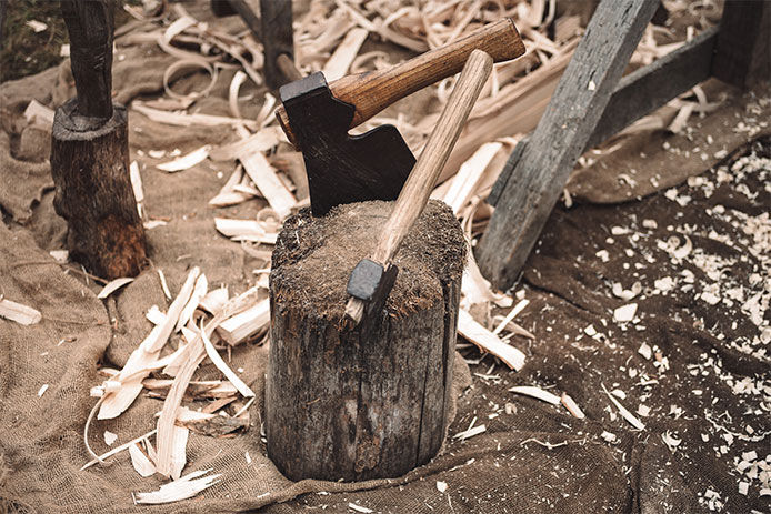 An axe stuck into a tree stump with chopped wood surrounding