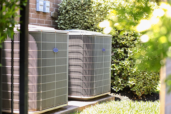 Air conditioner unit outdoors in side yard of a brick home in hot summer season. No people.