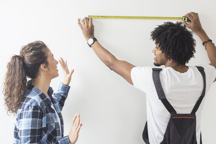 Young man meausring the wall, while a young woman is standing next to him. Both about 25 years old, African male and Caucasian female.