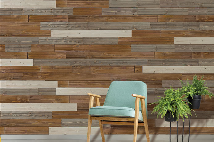 Gray, brown and white shiplap pieces being used to accent a living room wall. There is a blue modern chair and two fern plants in the foreground of the image.