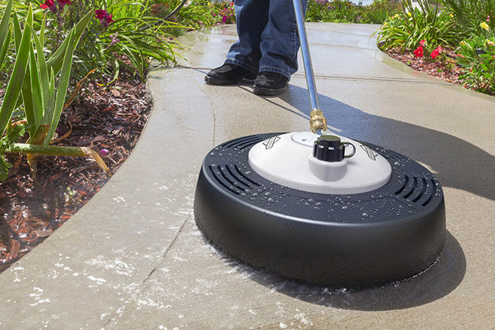 A man using a cement pavement pressure washer accessory to wash his sidewalk that is lined with colorful flowers