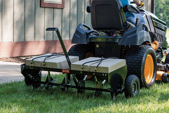 A man aerating his lawn with a aerator attached to his riding lawn mower