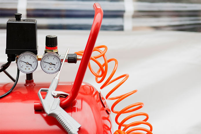 A close up of a red air compressor with two pressure gauges and a air tool laying on top of the compressor