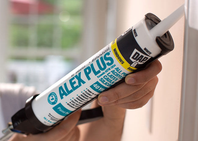 A close up image of a person using DAP Alex Plus in a caulking gun.