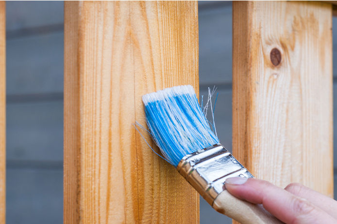 Using a nylon paint brush to apply stain to a wood fence panel 
