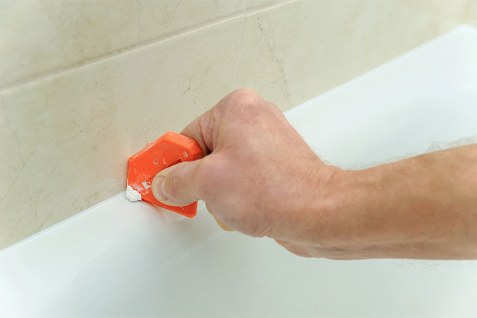Worker smoothing silicone sealant between the bath and the wall using a spatula.