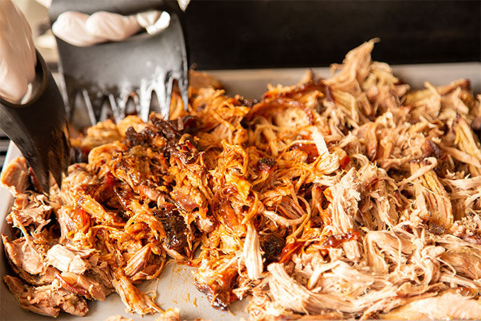 A person using meat shredders to shred up pork for pulled pork sandwiches