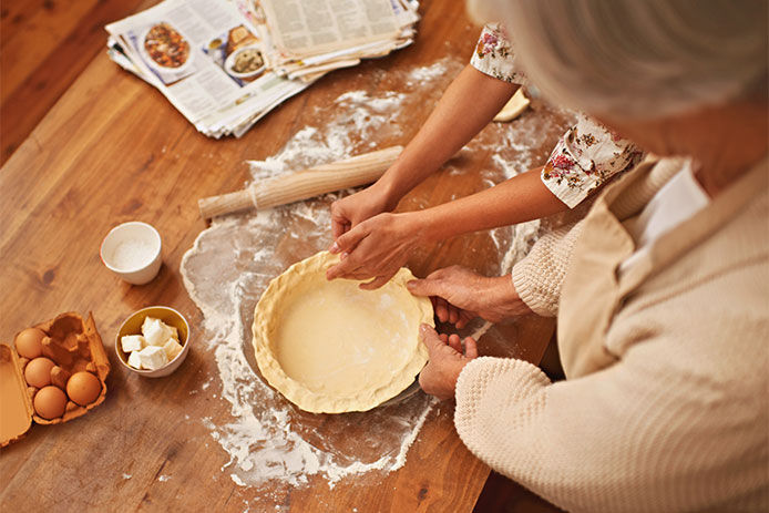 Woman and granddaughter pinching the pie dough to the pan to shape the crust