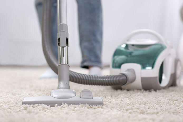 Person cleaning their beige carpet with a vacuum cleaner