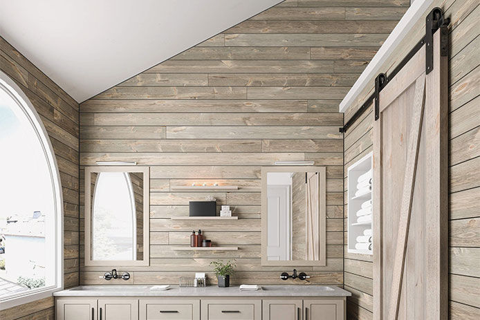 A modern bathroom with a beautiful curved window. The bathroom walls are lined with gray shiplap and a sliding bard door. The bathroom has accents of green foliage and white towels.