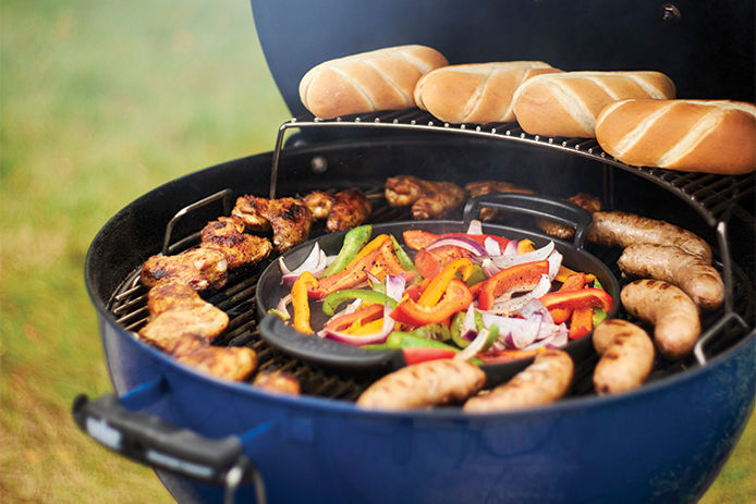 Blue Weber charcoal grill with brats, chicken, seasoned vegetables, and buns cooking 