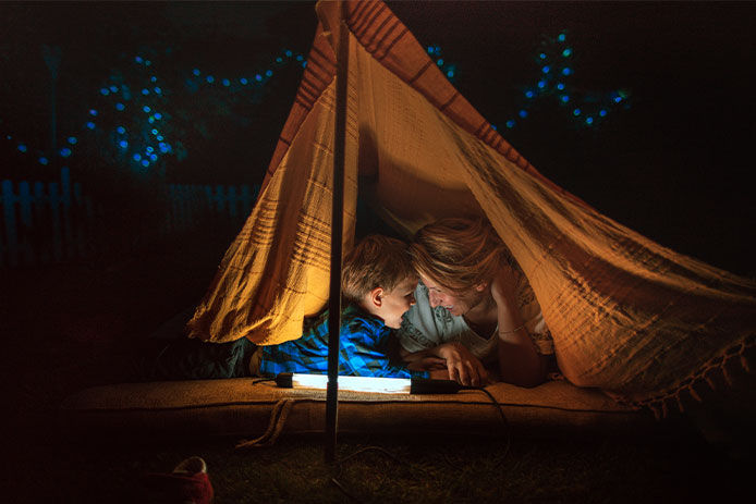 A mom and her son in a blanket fort outside