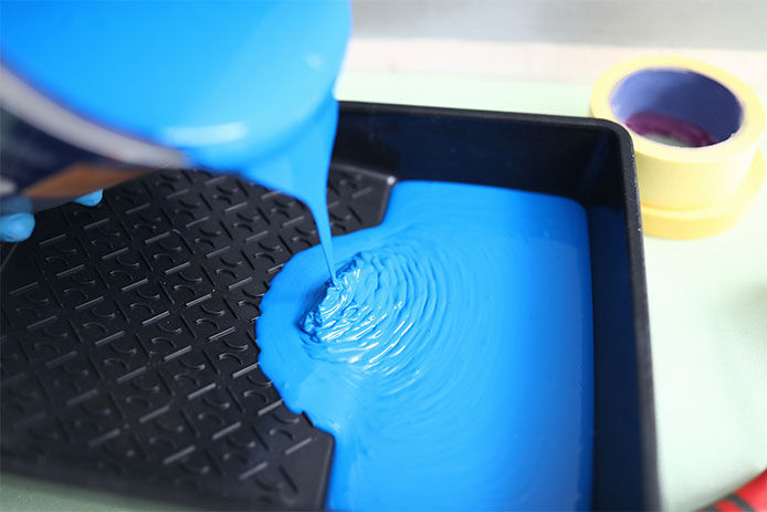 Blue paint being poured into a paint tray