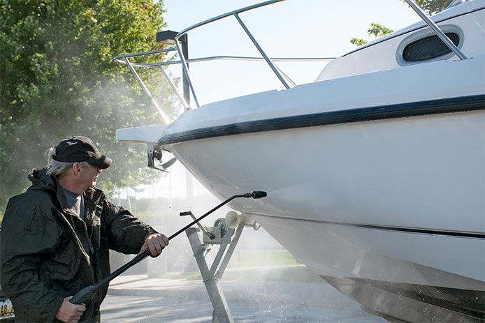 Older caucasian man using pressure washer to clean boat hull