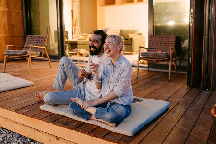 Photo of a young couple drinking wine by the fire pit in front of the cabin house