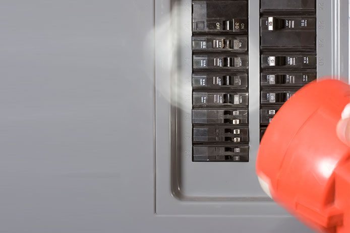 A grey-colored circuit breaker box is shown with black switches. A red flashlight shines on the switches to highlight them.