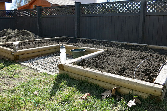 Raised garden bed made out of wood pieces filled with soil in backyard by fence