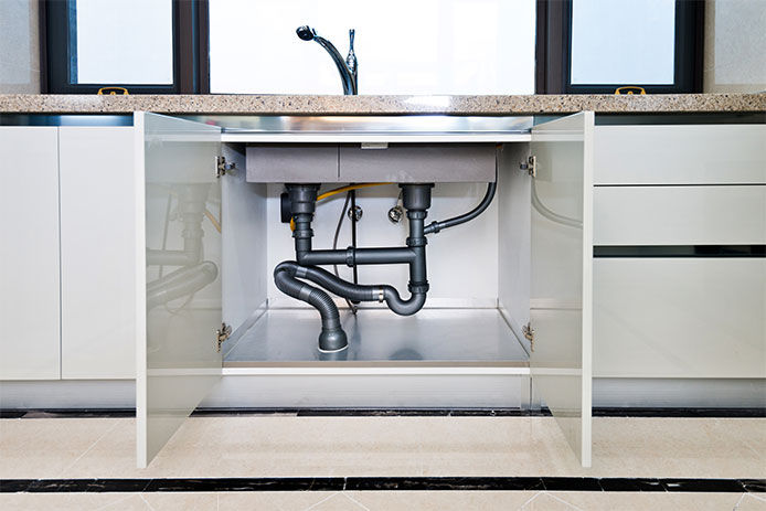 Open cabinet showing the water pipes under kitchen sink 