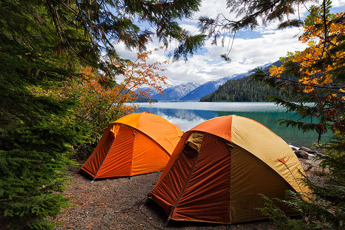 A couple of orange tents tucked in the trees with a view overlooking a lake and mountains in the background