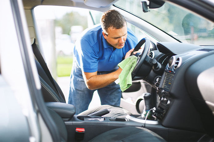 A man using a microfiber cloth to clean the interior of his car 
