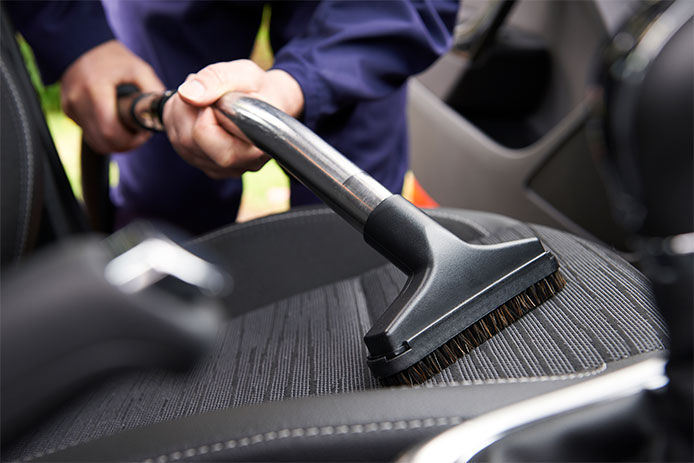 A man using a vacuum to clean the interior of his car