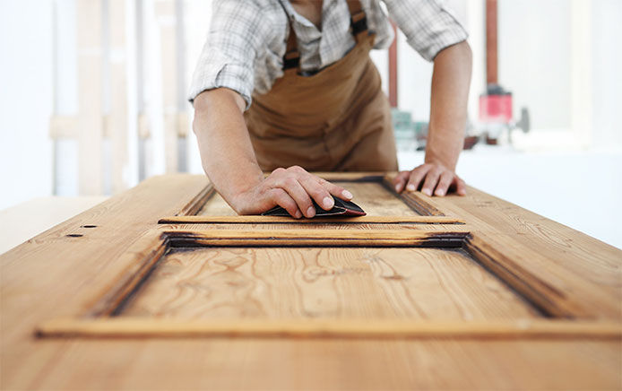 A carpenter working a wood door with the sandpaper while wearing a brown apron