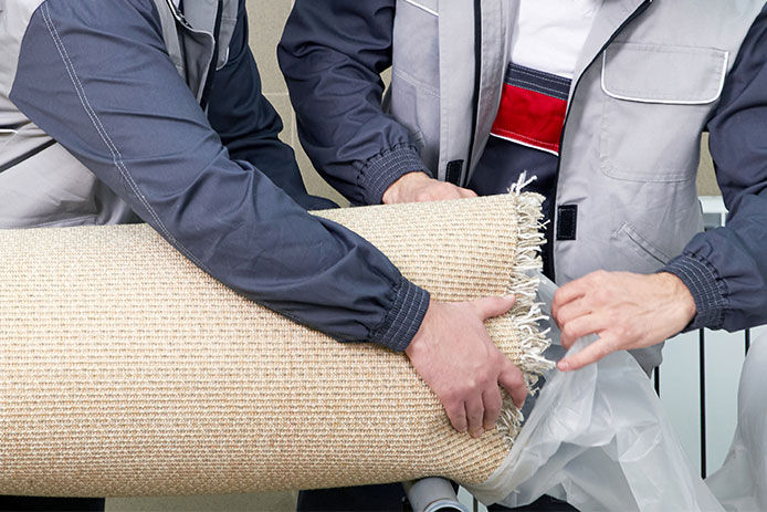 Two people trying to put a roll of old carpet into a clear garbage bag