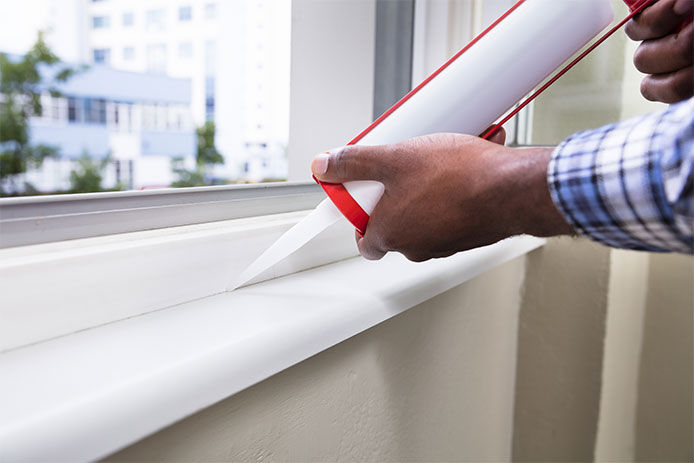 A professional homeowner using caulk to seal up windows in his home