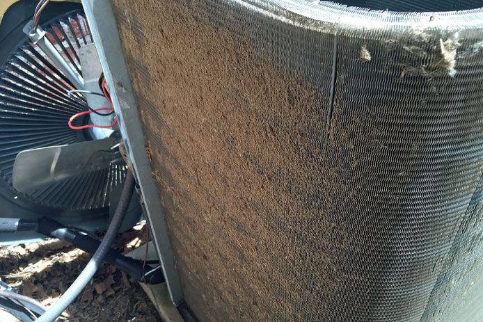Dirty condenser coil fins on a home air conditioner compressor in need of cleaning and maintenance by technician.