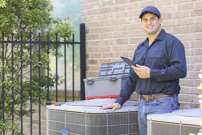 Latin descent blue collar air conditioner repairman working at residential home. He prepares to begin work by gathering appropriate tools and referring to digital tablet.