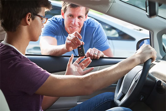 A father handing over keys to his son as he is learning how to drive 