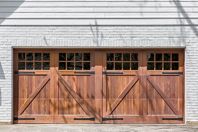 A wooden double garage door on a white brick house