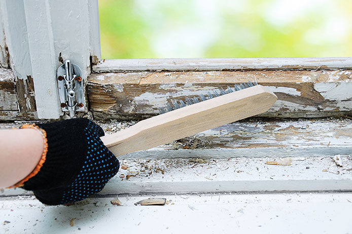 Brush with metal bristles in hand to remove old paint from the window.